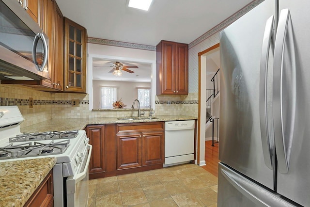 kitchen featuring glass insert cabinets, light stone counters, decorative backsplash, stainless steel appliances, and a sink