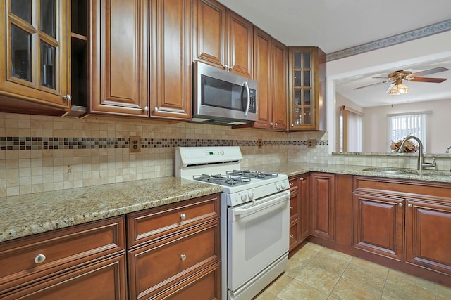 kitchen featuring white gas stove, stainless steel microwave, light stone countertops, and a sink