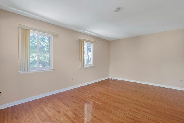 spare room with a wealth of natural light, light wood-type flooring, and baseboards