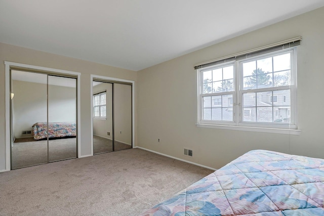 carpeted bedroom with baseboards, visible vents, and two closets