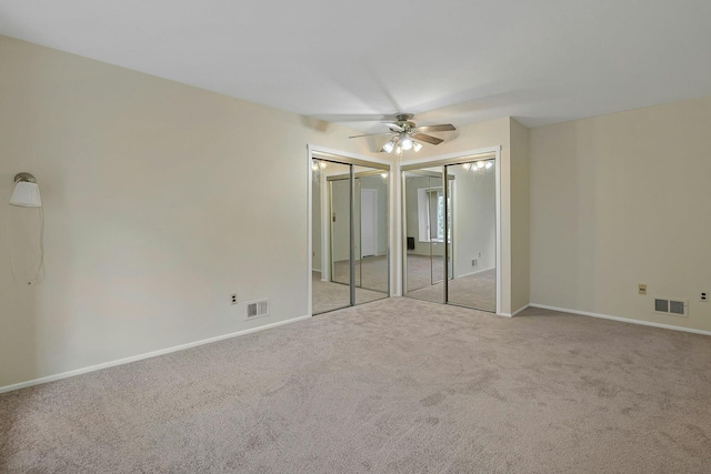 unfurnished bedroom with visible vents, baseboards, two closets, and carpet flooring