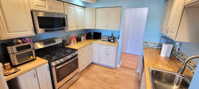 kitchen with light wood-type flooring, sink, appliances with stainless steel finishes, white cabinets, and wooden counters