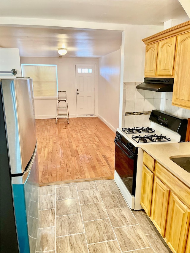 kitchen featuring light hardwood / wood-style flooring, light brown cabinetry, decorative backsplash, stainless steel fridge, and gas range oven