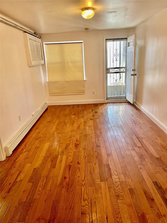 spare room featuring an AC wall unit, light wood-type flooring, and a baseboard heating unit