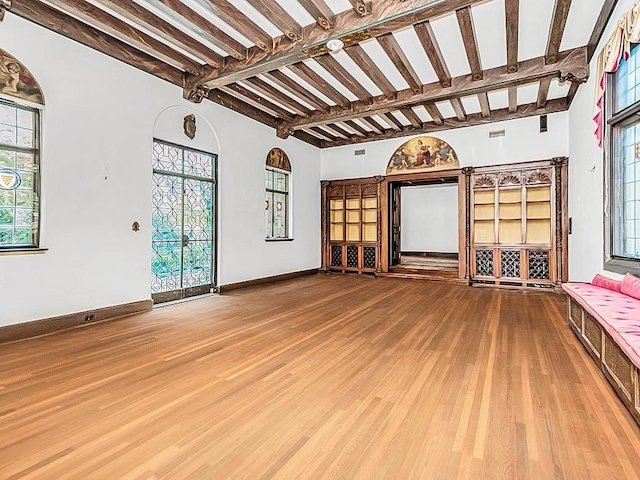 unfurnished living room featuring beamed ceiling, a wealth of natural light, and hardwood / wood-style floors