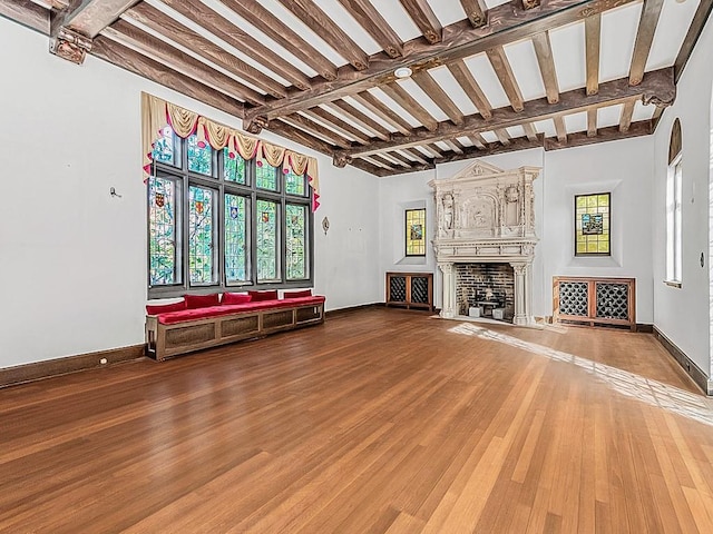 unfurnished living room with hardwood / wood-style floors, beamed ceiling, and a large fireplace