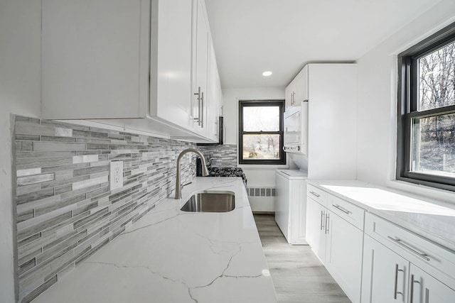 kitchen featuring white cabinetry, light stone countertops, backsplash, and sink