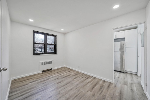 spare room featuring radiator and light hardwood / wood-style flooring