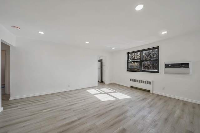 empty room featuring light wood-type flooring, an AC wall unit, and radiator heating unit