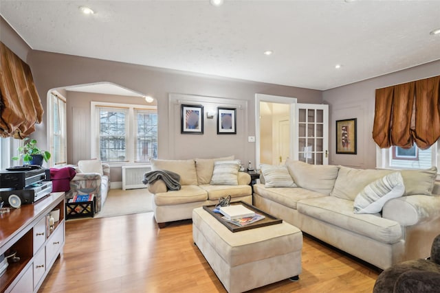 living area with arched walkways, radiator heating unit, light wood-type flooring, and recessed lighting