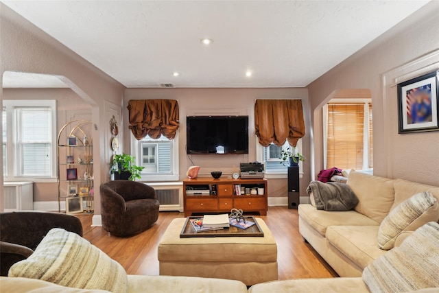 living area featuring light wood-type flooring, baseboards, arched walkways, and recessed lighting