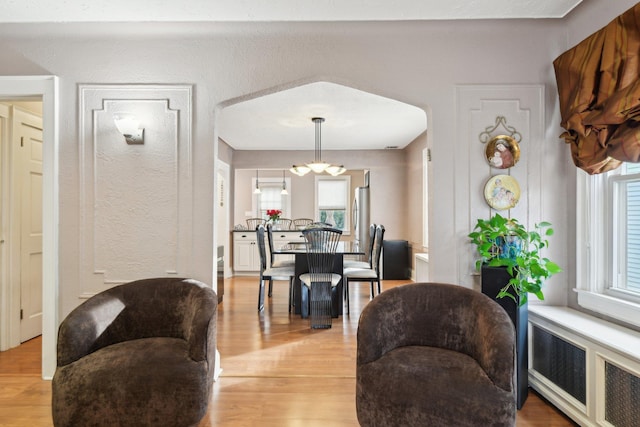 dining room featuring arched walkways, radiator heating unit, and light wood-style floors