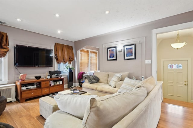 living room featuring light wood finished floors, visible vents, arched walkways, radiator, and recessed lighting