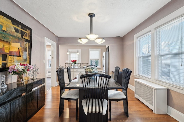 dining space featuring radiator, light wood-type flooring, baseboards, and a textured ceiling