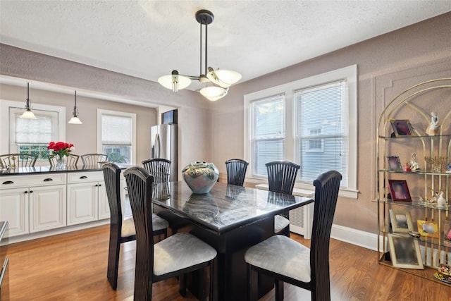 dining space with a chandelier, baseboards, a textured ceiling, and light wood finished floors