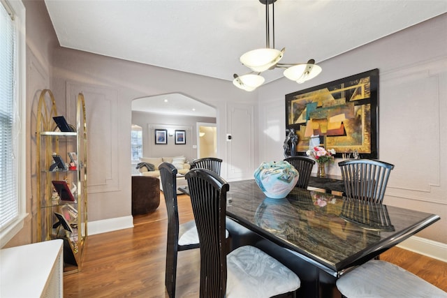 dining room with arched walkways, baseboards, and wood finished floors