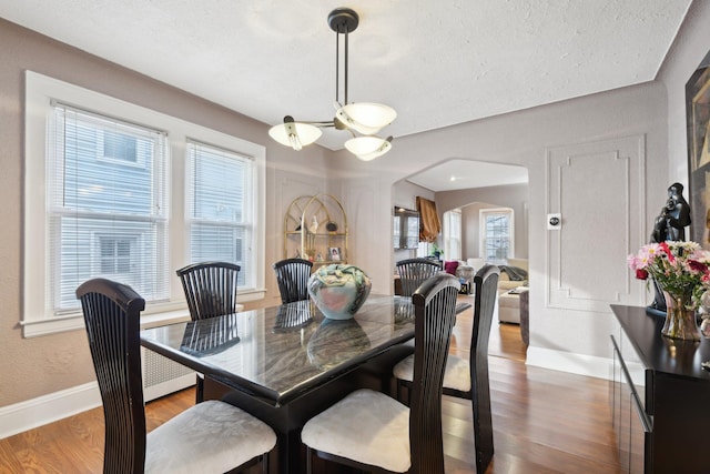 dining area featuring arched walkways, a textured ceiling, dark wood finished floors, and baseboards