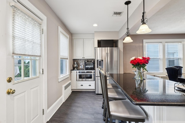 kitchen featuring a breakfast bar, pendant lighting, stainless steel appliances, visible vents, and white cabinetry