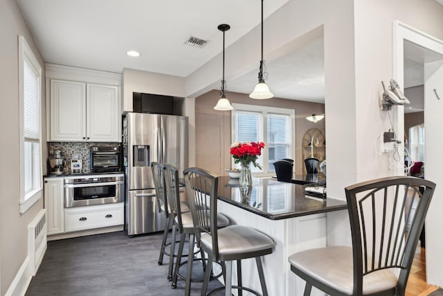 kitchen with visible vents, hanging light fixtures, appliances with stainless steel finishes, white cabinetry, and a peninsula