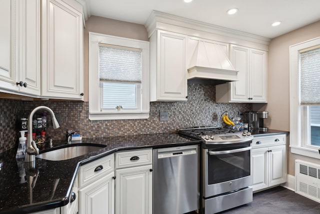 kitchen with a sink, white cabinetry, appliances with stainless steel finishes, custom exhaust hood, and radiator