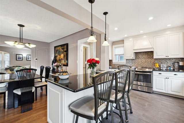 kitchen featuring dark countertops, hanging light fixtures, stainless steel range oven, white cabinetry, and premium range hood