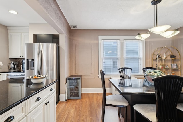 kitchen featuring visible vents, hanging light fixtures, white cabinetry, dark stone counters, and beverage cooler