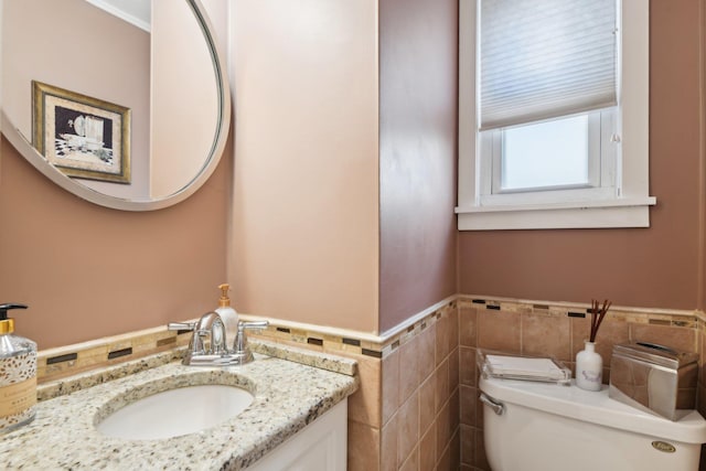 bathroom with a wainscoted wall, vanity, toilet, and tile walls