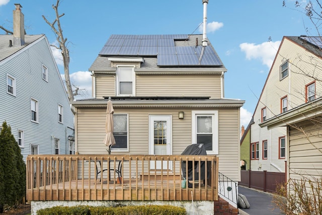 back of property featuring a shingled roof, roof mounted solar panels, fence, and a wooden deck