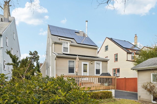 back of house with roof mounted solar panels, fence, and a deck