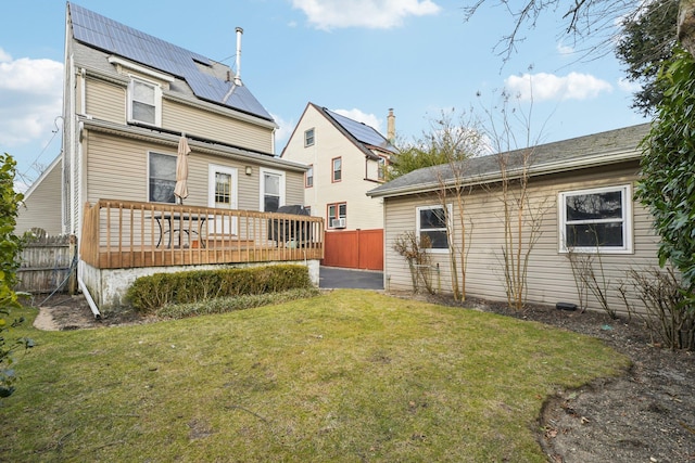 rear view of property with a yard, roof mounted solar panels, fence, and a wooden deck