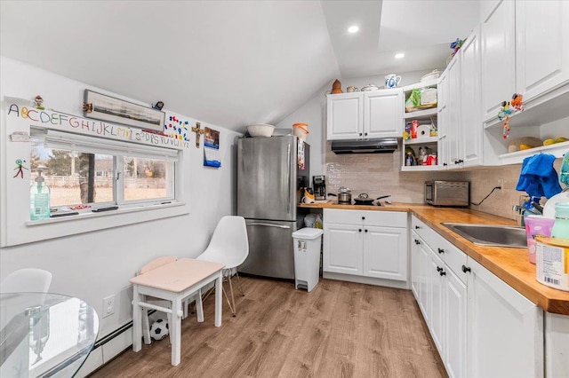 kitchen with lofted ceiling, under cabinet range hood, a sink, freestanding refrigerator, and open shelves