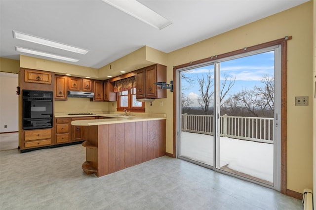 kitchen with a baseboard radiator, gas stovetop, sink, oven, and kitchen peninsula