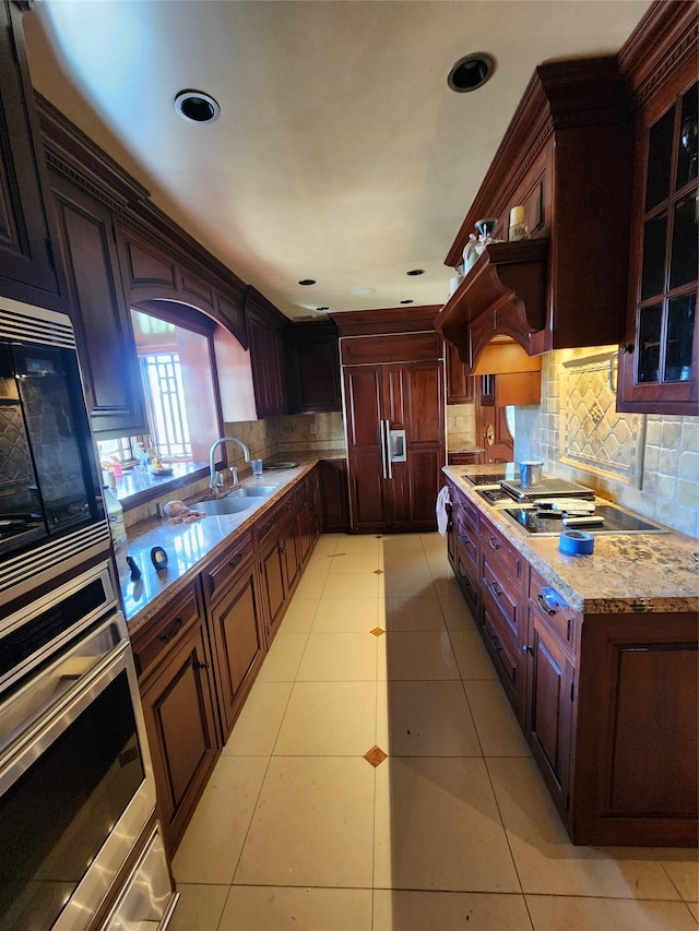 kitchen featuring built in appliances, sink, light stone counters, light tile patterned flooring, and decorative backsplash