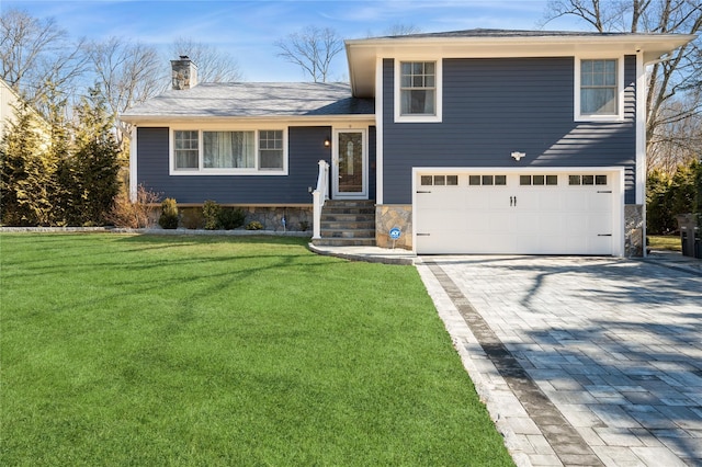 tri-level home with a garage, a chimney, decorative driveway, and a front yard