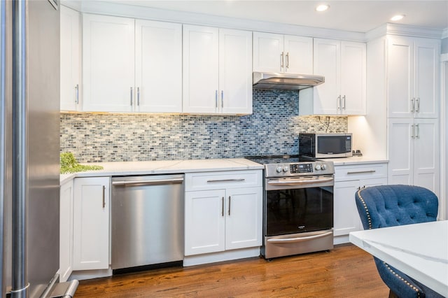 kitchen with under cabinet range hood, wood finished floors, white cabinetry, appliances with stainless steel finishes, and tasteful backsplash