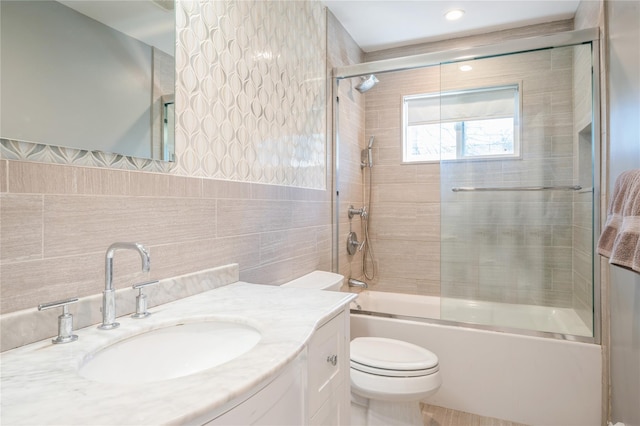 bathroom featuring bath / shower combo with glass door, vanity, toilet, and tile walls