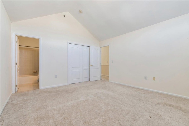 unfurnished bedroom featuring connected bathroom, light colored carpet, high vaulted ceiling, and a closet