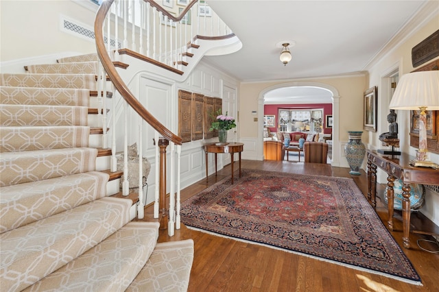 entryway with wood finished floors, arched walkways, wainscoting, crown molding, and a decorative wall