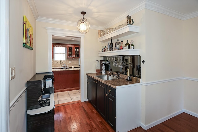 bar featuring sink, ornamental molding, tasteful backsplash, dark stone countertops, and dark hardwood / wood-style floors