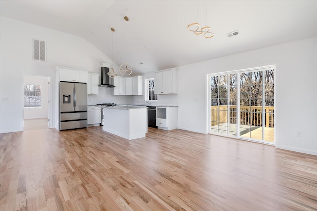 kitchen featuring wall chimney range hood, appliances with stainless steel finishes, white cabinetry, and pendant lighting