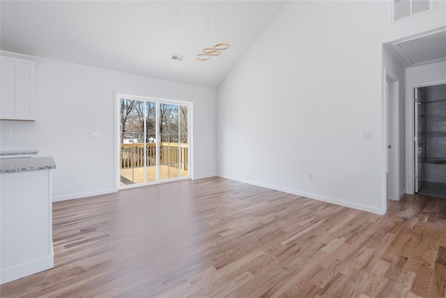 unfurnished dining area with light wood-type flooring and high vaulted ceiling