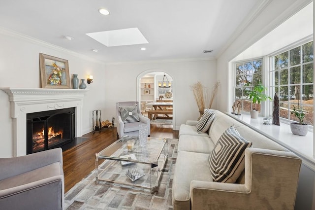 living area with a warm lit fireplace, ornamental molding, arched walkways, and wood finished floors