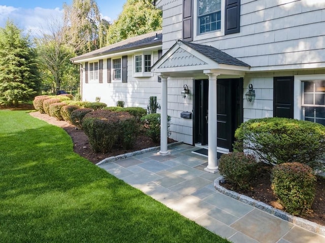 property entrance with a shingled roof, a patio, and a yard