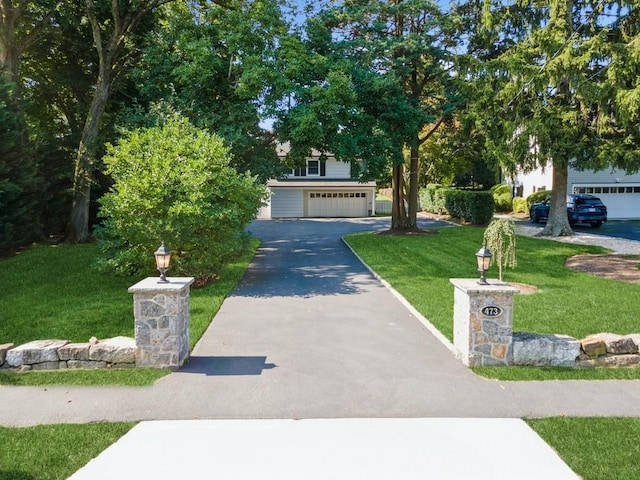 view of property hidden behind natural elements featuring a garage, aphalt driveway, and a front lawn