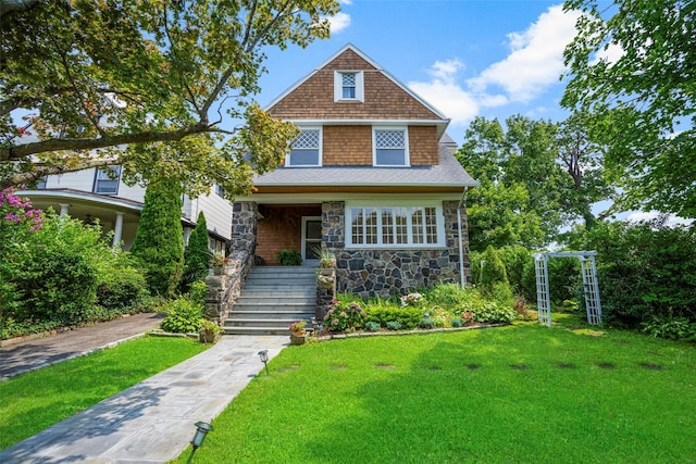 shingle-style home featuring stone siding, a front lawn, and roof with shingles