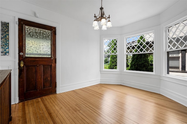 foyer entrance featuring baseboards, light wood-style flooring, and an inviting chandelier