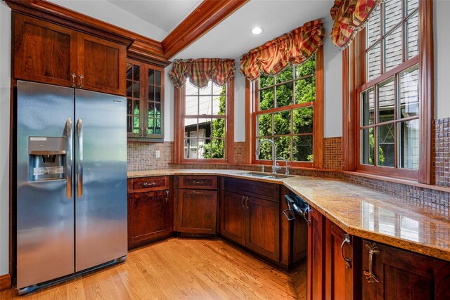 kitchen featuring light stone counters, stainless steel refrigerator with ice dispenser, light wood finished floors, decorative backsplash, and a sink