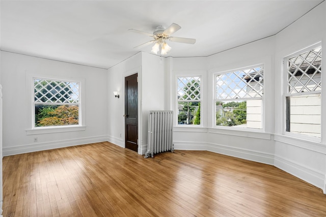 interior space with light wood-type flooring, baseboards, ceiling fan, and radiator heating unit