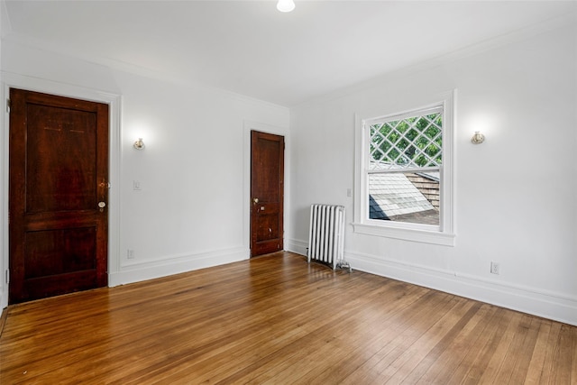 spare room featuring radiator heating unit, baseboards, and wood-type flooring