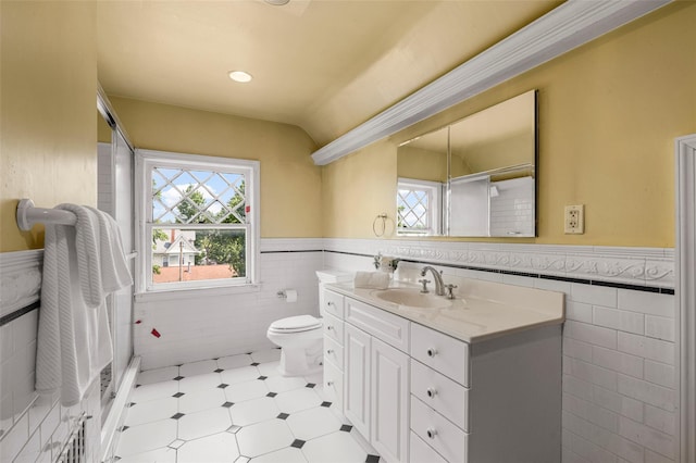 bathroom with tile walls, toilet, wainscoting, vaulted ceiling, and vanity